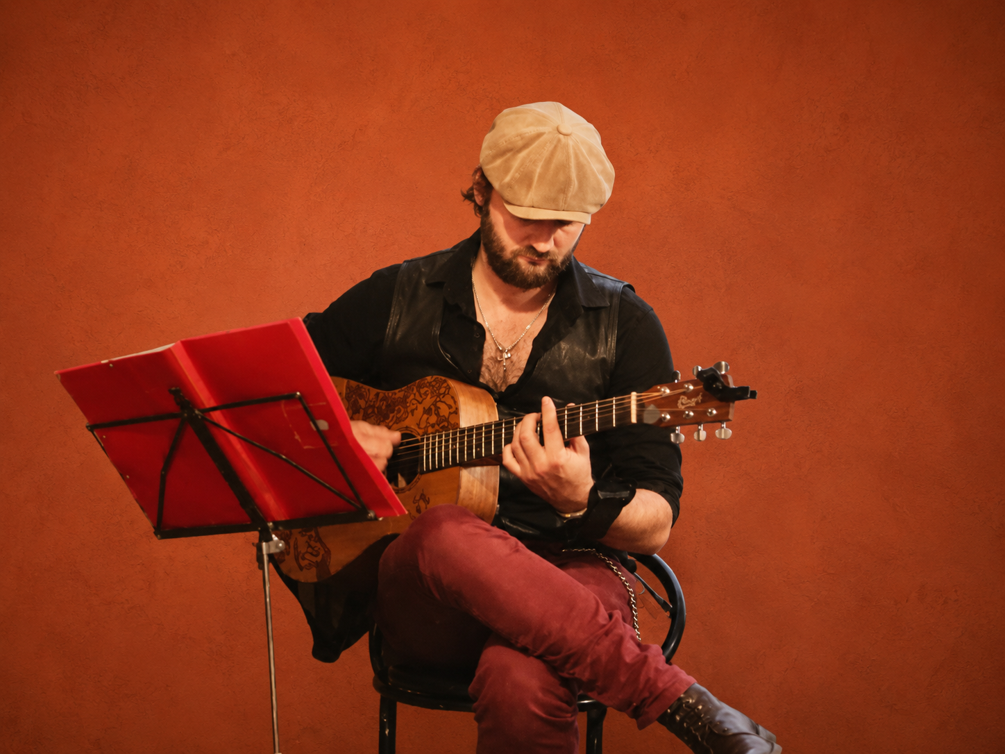 Marty en concert, assis avec sa guitare devant son pupitre rouge, sur fond terracotta